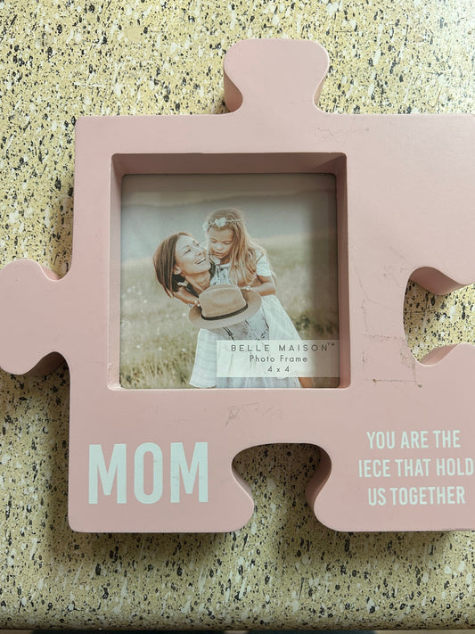 Pink puzzle piece-shaped photo frame with 'Mom' on a textured surface